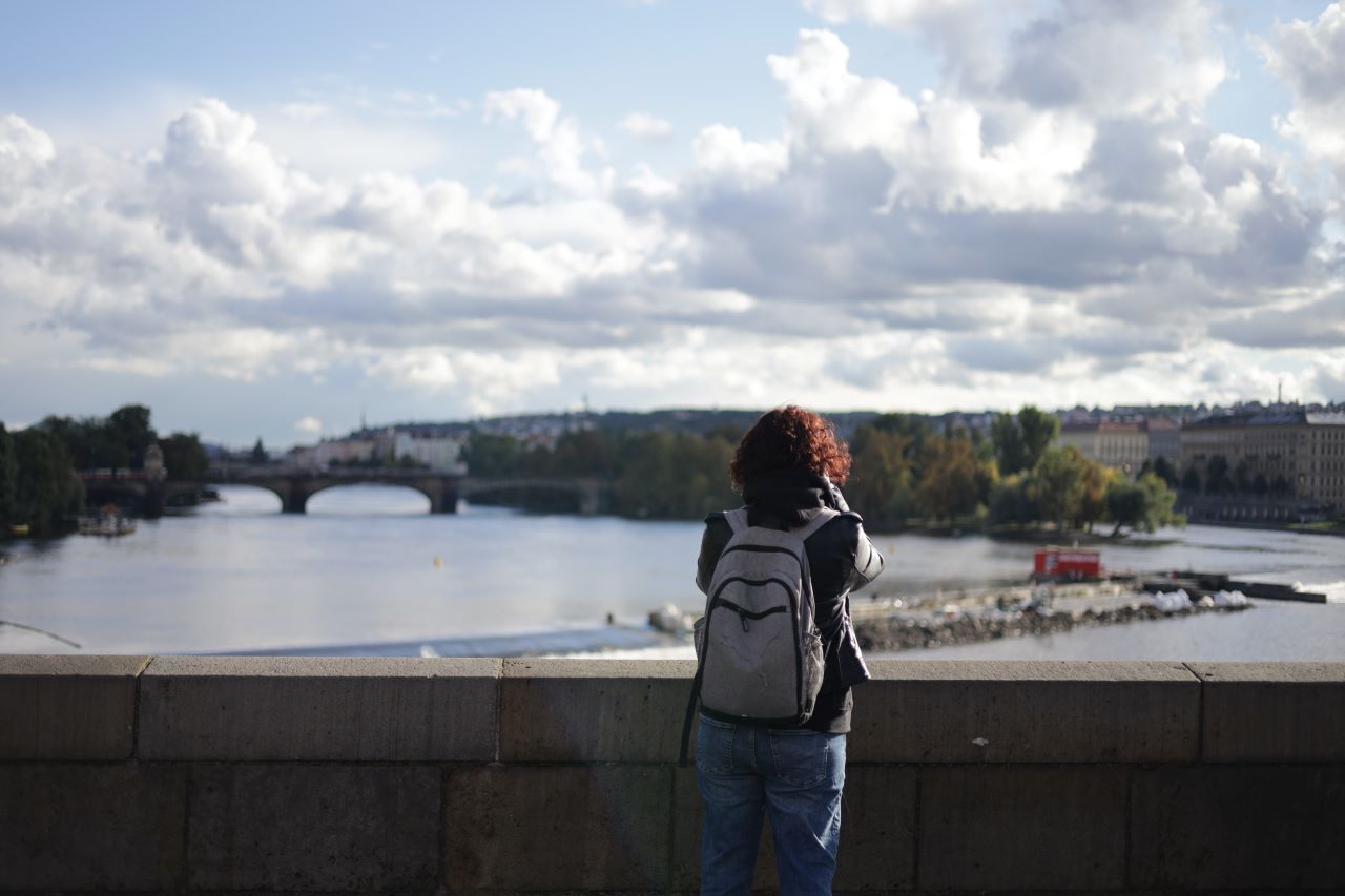 Na zdjęciu kobieta na moście, w tle miasto Praga